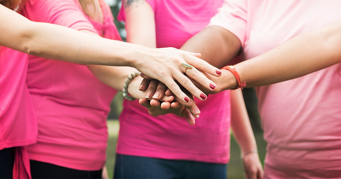 People in pink shirts have their hands out stacked on top of one another