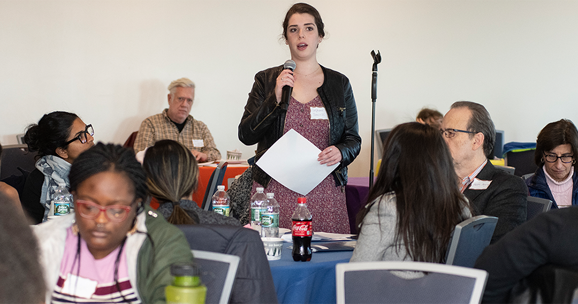 Person standing up at a table speaking into a microphone