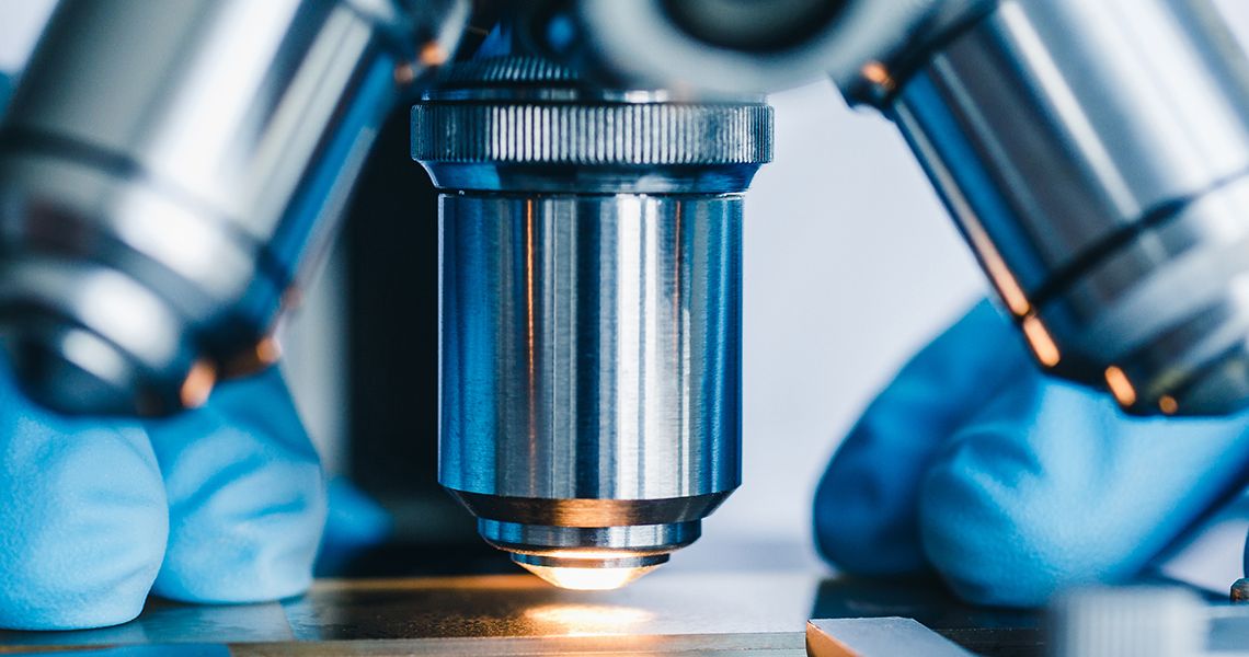 close-up of gloved hands working at a microscope